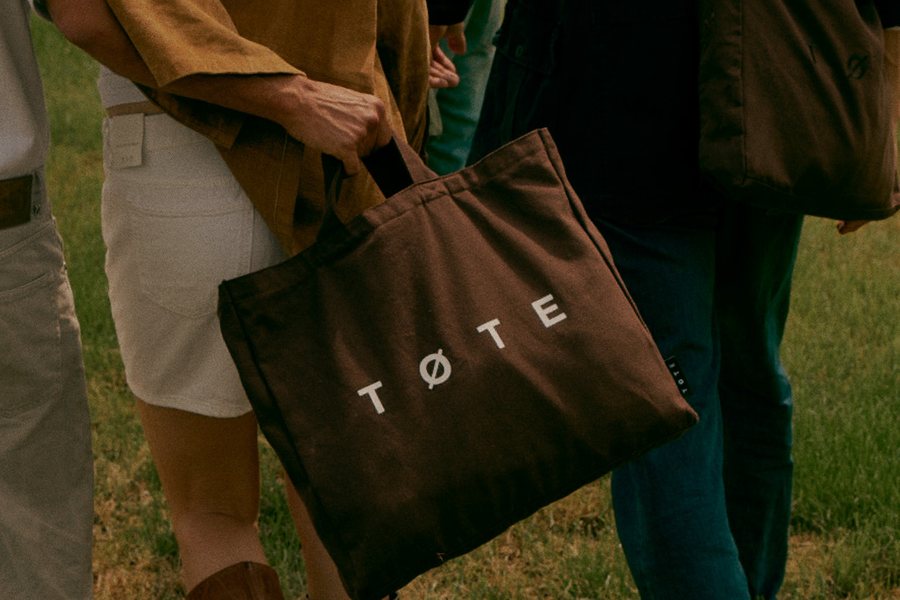 A brown TØTE bag carried by hand, with three people standing in a field